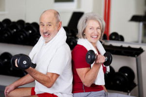 Senior Couple Lifting Dumbbells While Sitting In Gym