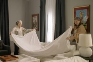 Two women collaborate in making a bed, showcasing teamwork across generations. — assisted living